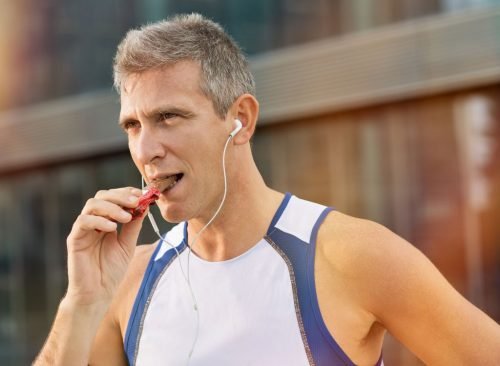 Les hommes qui mangent des barres de protéines ont des écouteurs pendant l'entraînement