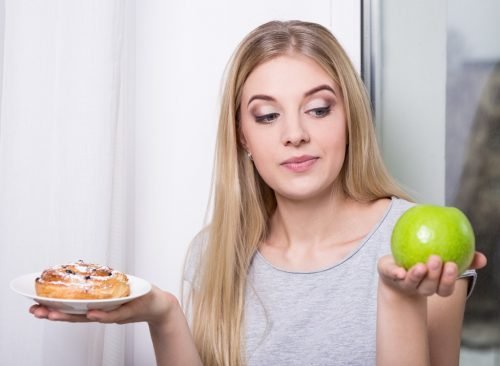 Femme choisissant pomme au-dessus d'une pâtisserie au sucre - perte de poids malsaine