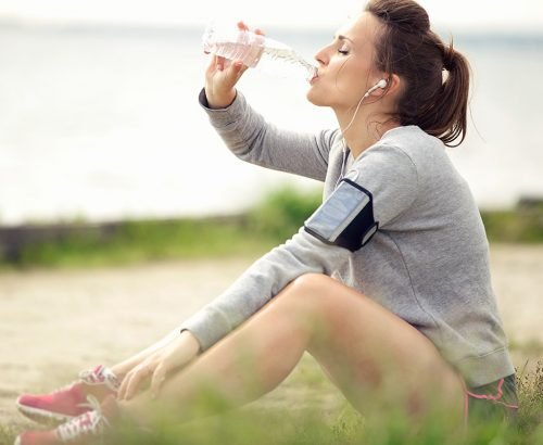 Femme assise dans l'herbe buvant à une bouteille d'eau après l'exercice