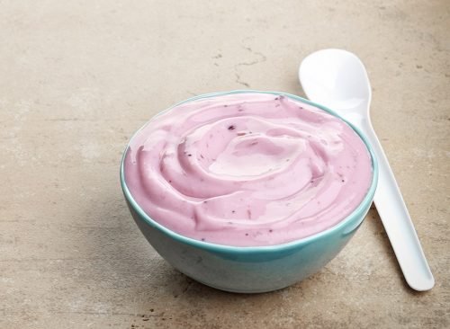 Yaourt à la fraise rose dans un bol en céramique bleu et une cuillère blanche