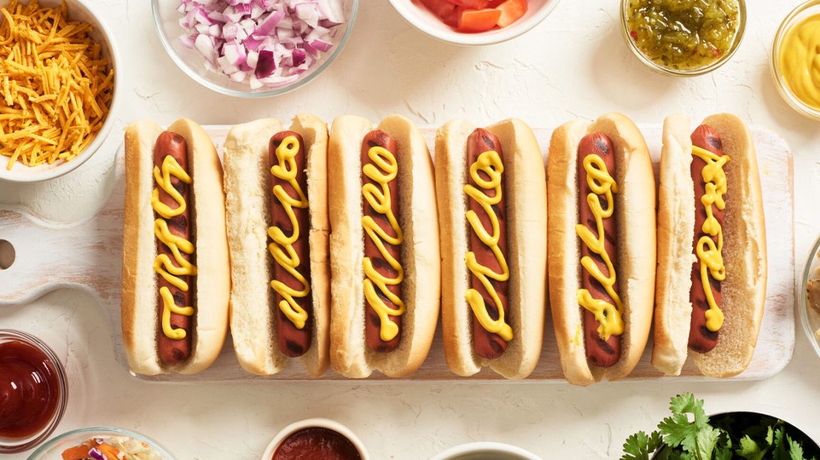 Six hot-dogs sur une table entourée de condiments