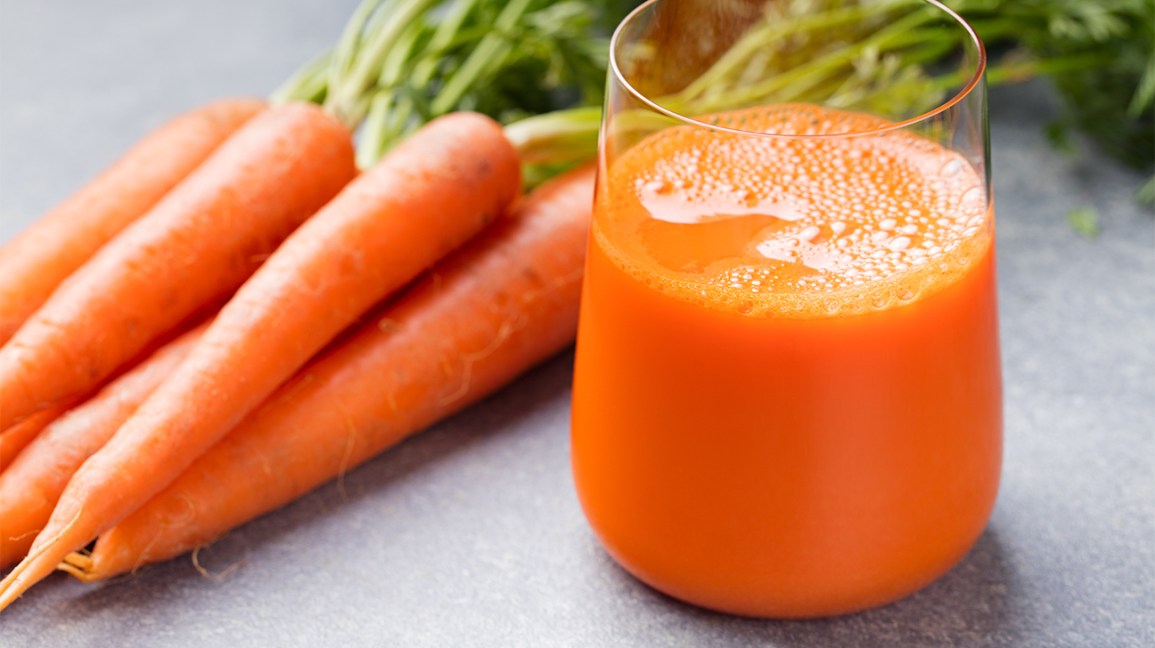 un verre de jus de carotte à côté de carottes