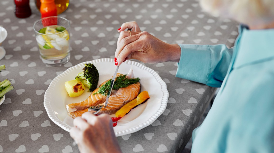 femme plus âgée, manger du saumon et des légumes