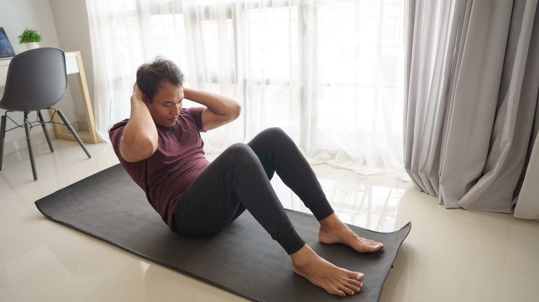 Homme sur un tapis de yoga à la maison faisant un sit-up