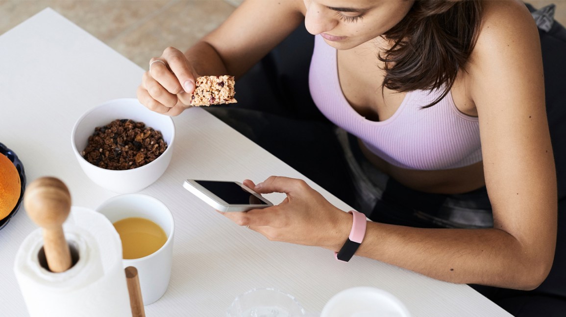 Femme au téléphone en train de manger une barre protéinée, du granola et du jus d'orange