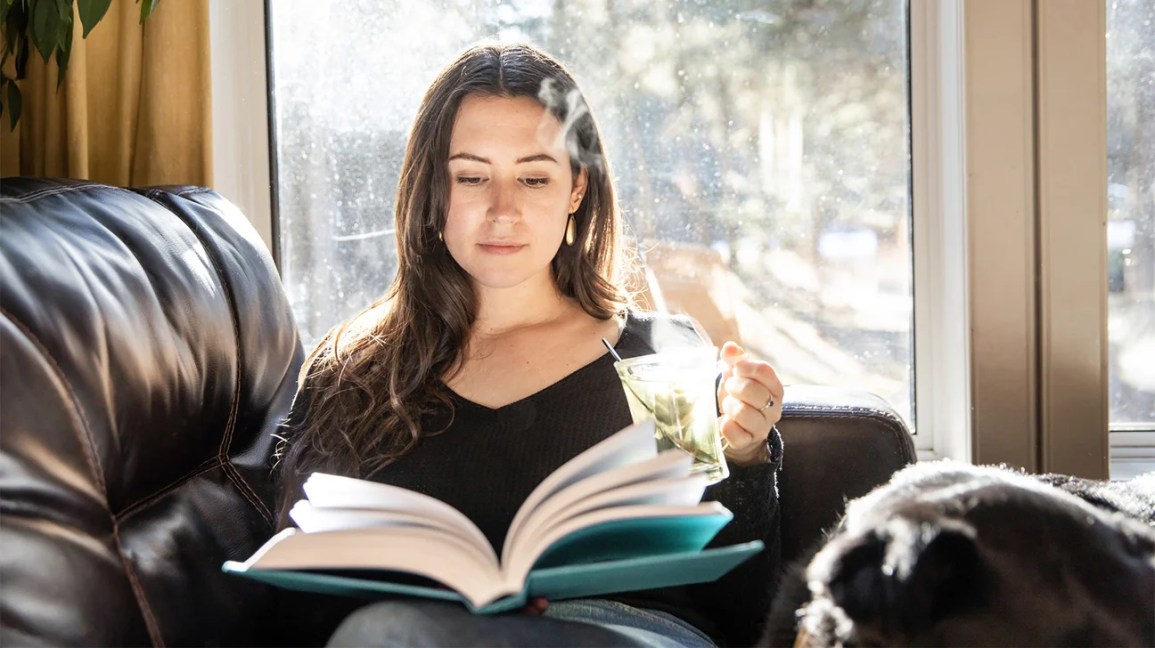 Une personne lit un livre sur son canapé tout en tenant une tasse en plastique de thé vert glacé.
