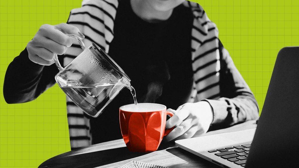 Image d'une personne versant de l'eau chaude dans une tasse alors qu'elle est assise devant un ordinateur portable