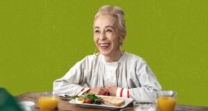 femme âgée souriante assise à table devant un service de livraison de repas pour personnes âgées, isolée sur fond vert