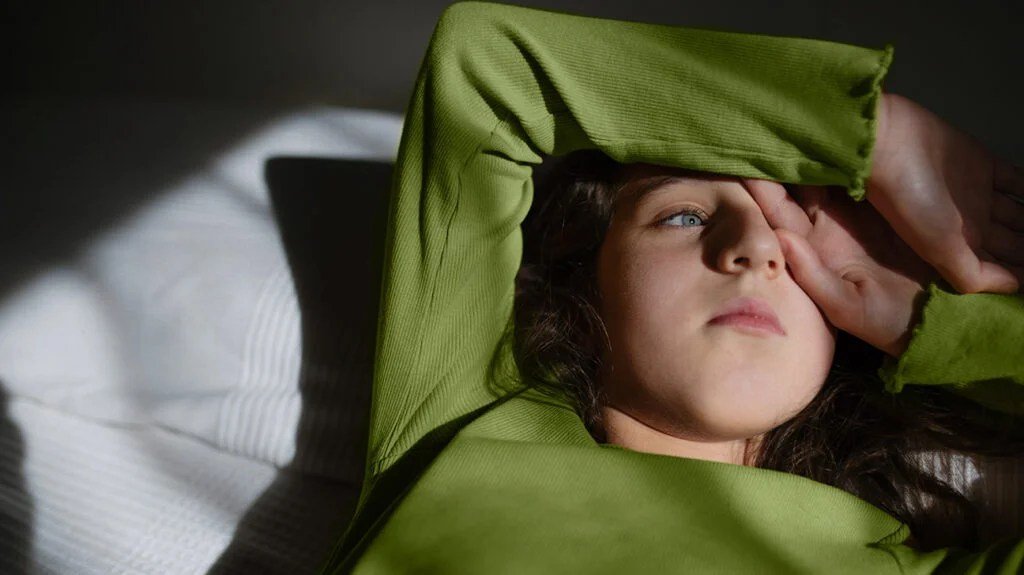 Una ragazza con un maglione verde sdraiata su un letto.