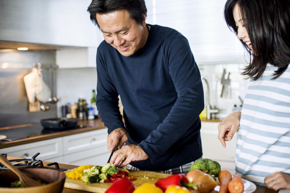 Pareja cortando verduras y cocinándolas en la cocina para la dieta paleo