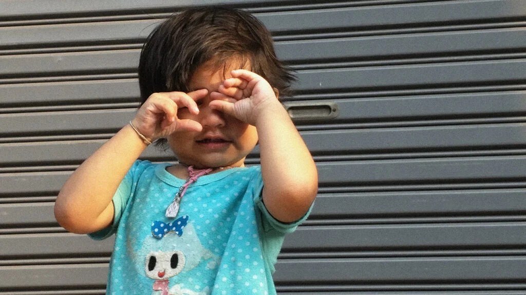 Fotografia di un bambino piccolo che indossa una maglietta blu e con le mani sugli occhi, per accompagnare un articolo sulle secrezioni oculari nei bambini piccoli.