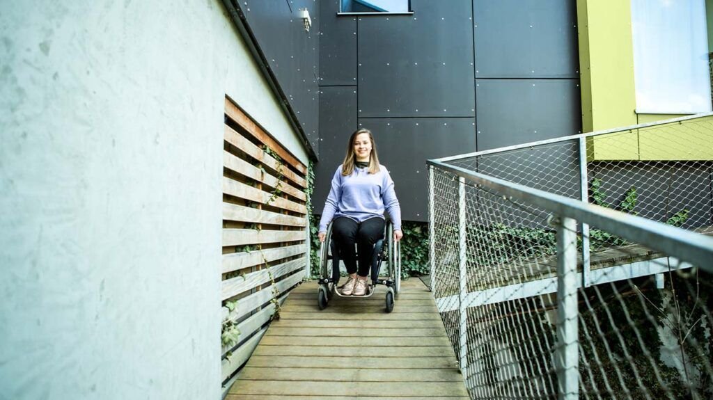 Une femme utilisant un fauteuil roulant pour descendre une rampe dans un bâtiment moderne.