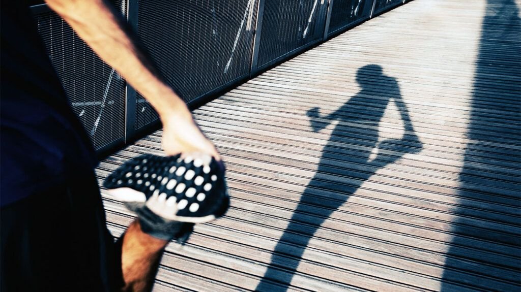 L'ombre d'un coureur faisant un étirement en quad debout et regardant sa montre intelligente