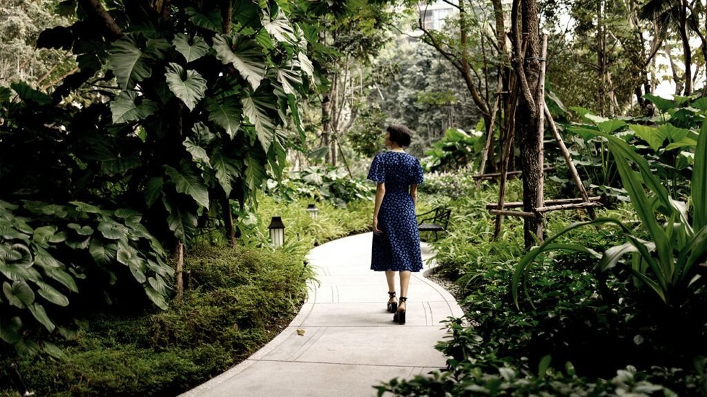 personne en robe bleue à pois blancs marchant dans une ruelle dans un parc verdoyant