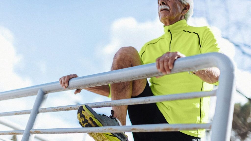 Un homme plus âgé en tenue de sport étend une jambe en haut sur une balustrade